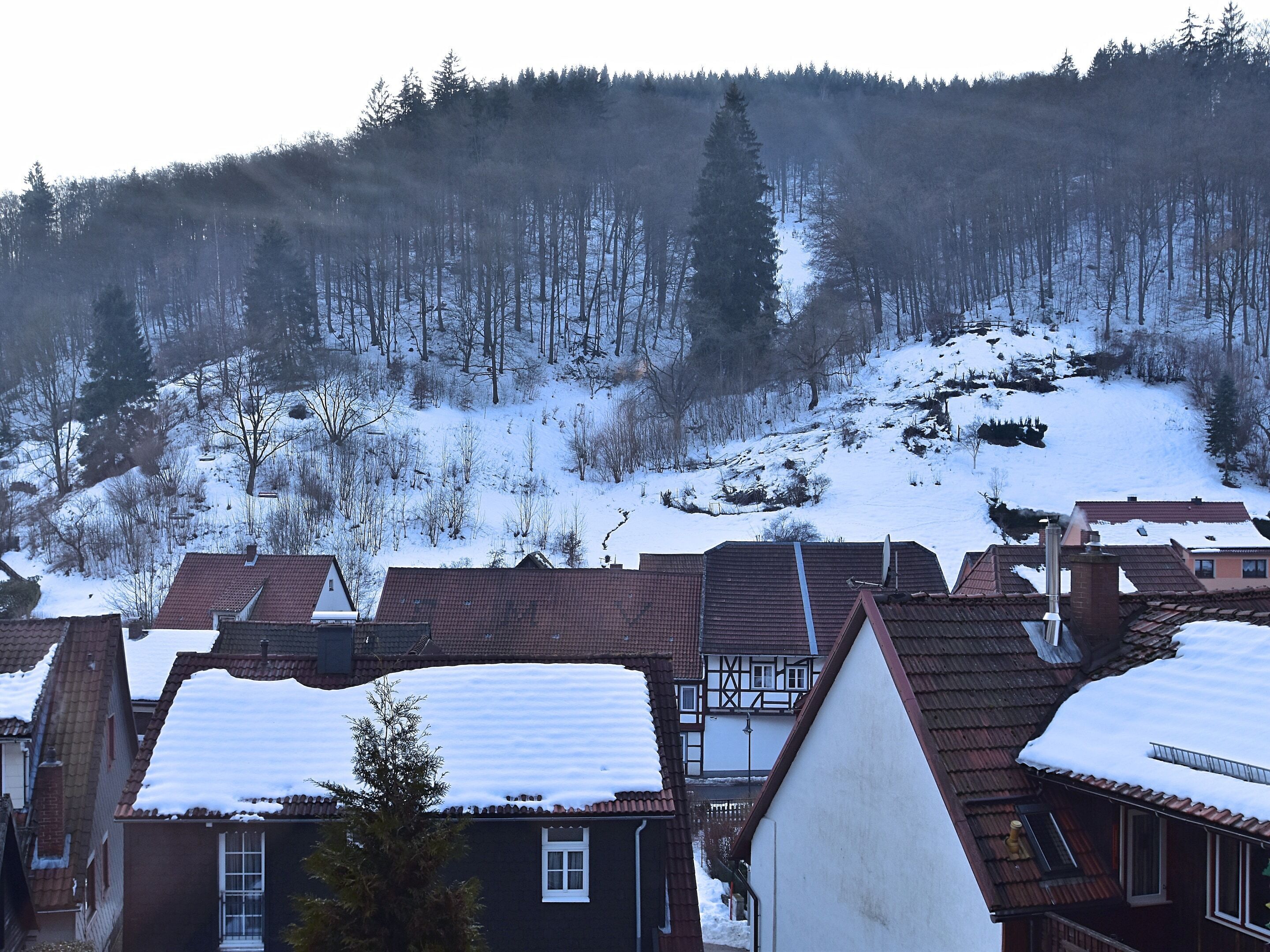 A residential area with houses having red-tiled roofs and snow-covered surroundings.
