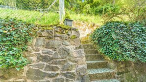 Una escalera de piedra que asciende por un sendero rocoso, rodeada de abundante vegetación y una cerca metálica.
