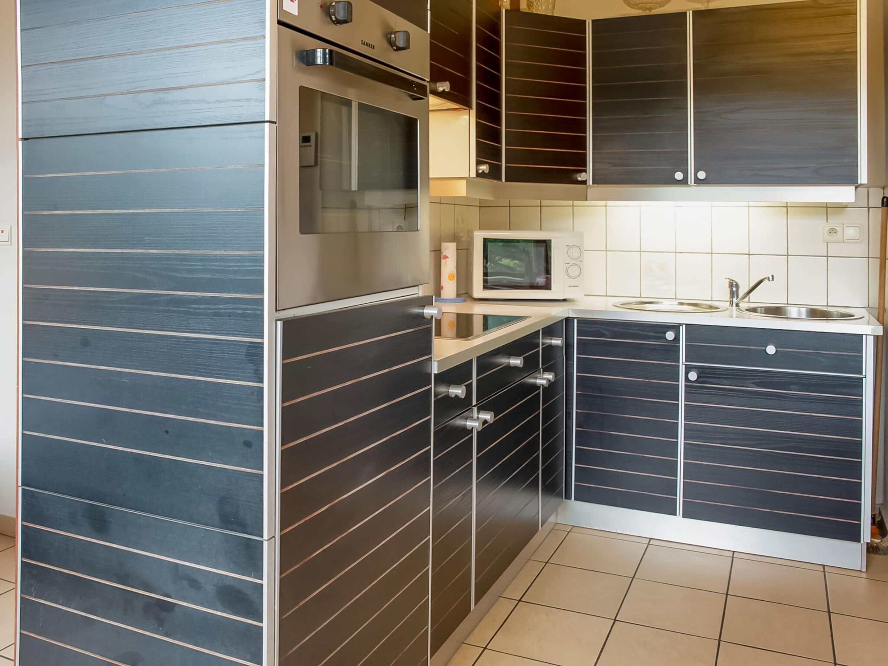 A compact kitchen with dark cabinetry, a built-in oven, a microwave, and a sink.