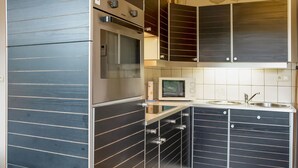 A compact kitchen with dark cabinetry, a built-in oven, a microwave, and a sink. - A Small Studio of a Nature Stone House (Aywaille)