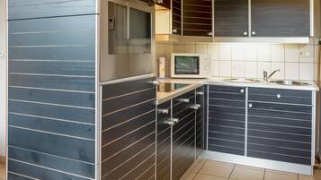 A compact kitchen with dark cabinetry, a built-in oven, a microwave, and a sink.