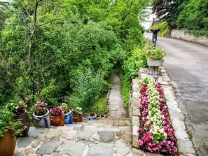 A stone pathway leading to a garden with potted plants and flowers. - A Small Studio of a Nature Stone House (Aywaille)
