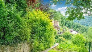 A lush garden with a stone wall, a pathway, and a building in the background. - A Small Studio of a Nature Stone House (Aywaille)