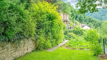 A lush garden with a stone wall, a pathway, and a building in the background.