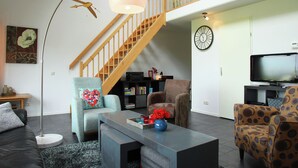 Ein Wohnzimmer mit Treppe, einer Couch, einem Couchtisch mit Dekoration und einem Fernseher.