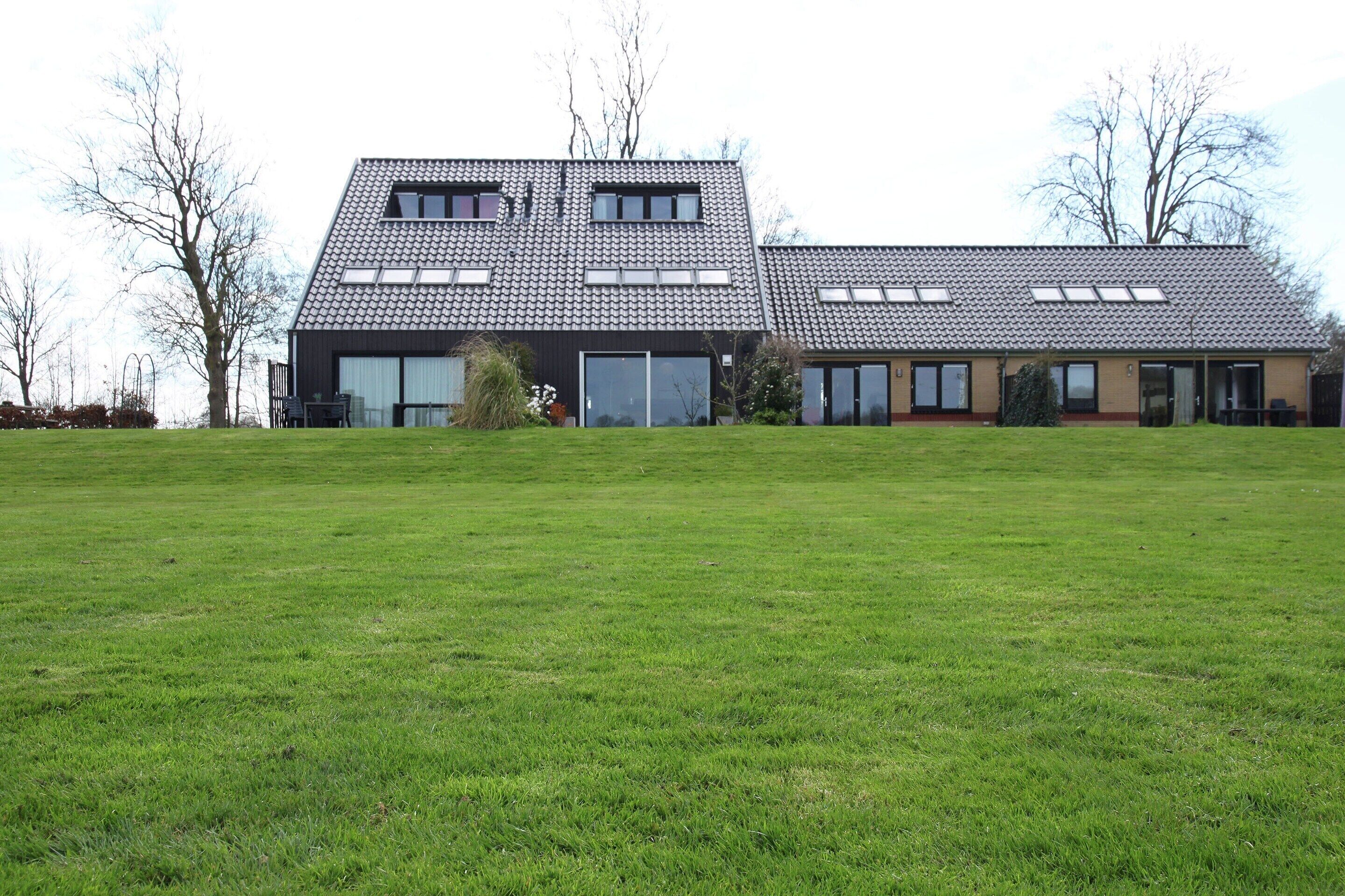 Une maison moderne à deux étages, dotée d’un toit en pente, de grandes fenêtres et d’une vaste pelouse à l’avant.