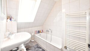 A modern bathroom with a white sink, a bathtub, and a towel rack. - Ferienzimmer in Kropelin (Kroepelin)