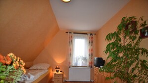 A small, cozy room with a bed, a nightstand, a lamp, a radiator, a television, and a potted plant. - Ferienzimmer in Kropelin (Kroepelin)