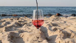 A glass of red drink with a straw on a sandy beach with the ocean in the background. - Ferienzimmer in Kropelin (Kroepelin)
