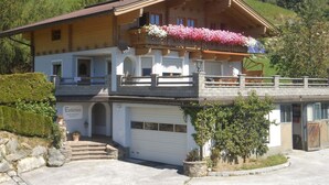 A two-story chalet with a balcony adorned with flowers, a garage, and a stone staircase leading to the entrance. - Comfy Apartment in Hollersbach im Pinzgau near Lake (Hollersbach im Pinzgau)