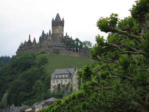 A castle-like building with multiple towers, surrounded by lush greenery and a smaller building with a sloped roof in the foreground. - Apartment in a Former Farmhouse (Mastershausen)
