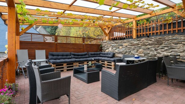 An outdoor patio with a wooden pergola, stone wall, and outdoor seating area. - Stylish Apartment in Merschbach near Forest (Merschbach)