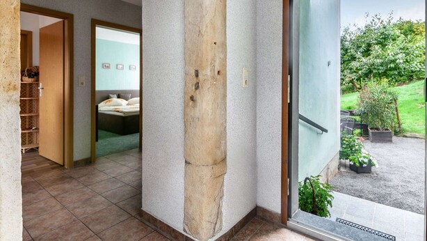 Een modern interieur met een stenen pilaar, een badkamer met een bad en uitzicht op een tuin door een glazen deur.