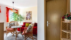 Een woonkamer met een rode bank, rieten stoelen, een ronde tafel en een houten deur.