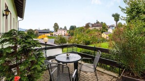 Een balkon met een ronde tafel en stoelen, met uitzicht op een groen landschap en gebouwen in de verte.