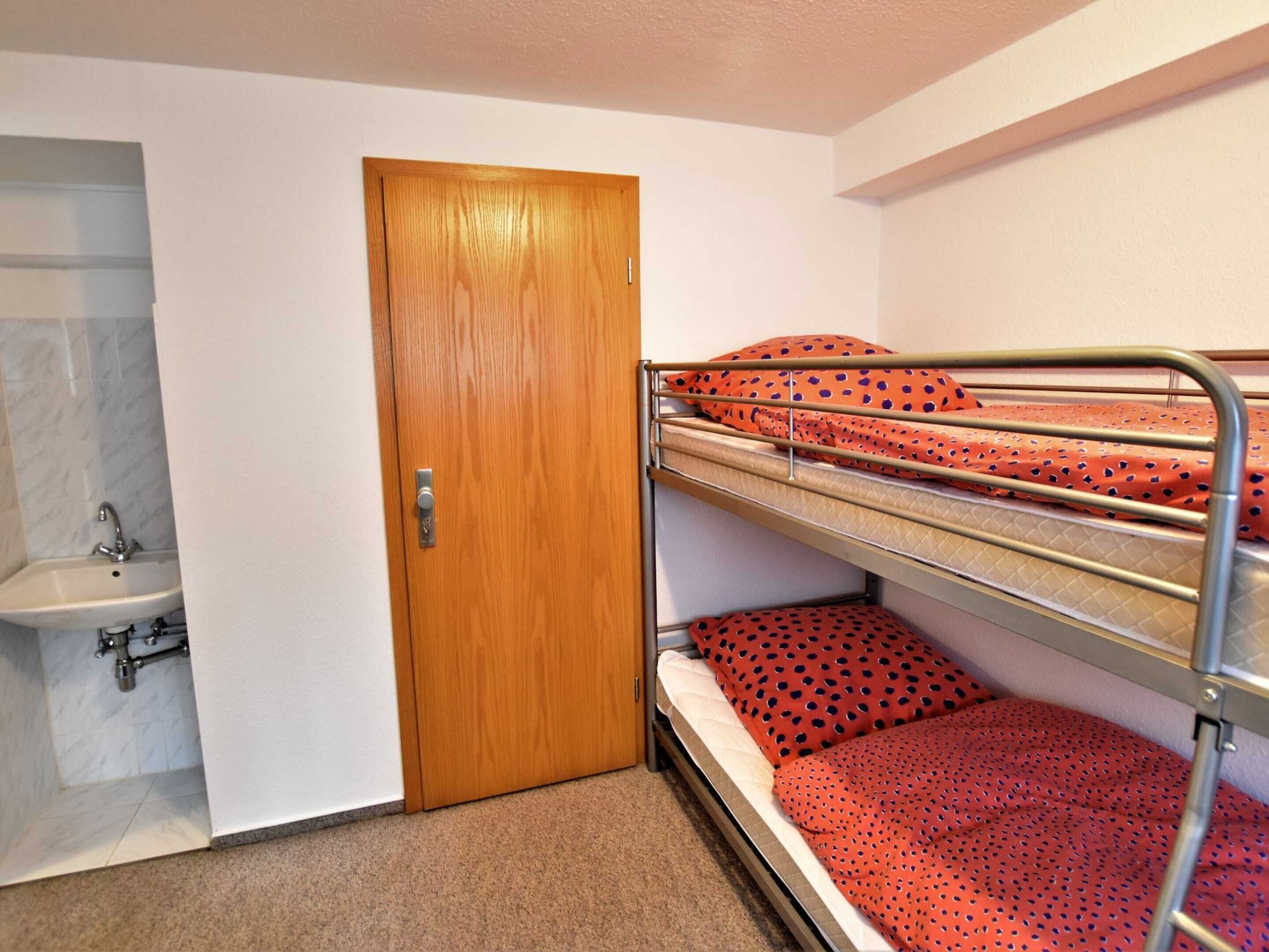 A bunk bed room with a wooden door, a sink, and a tiled wall.