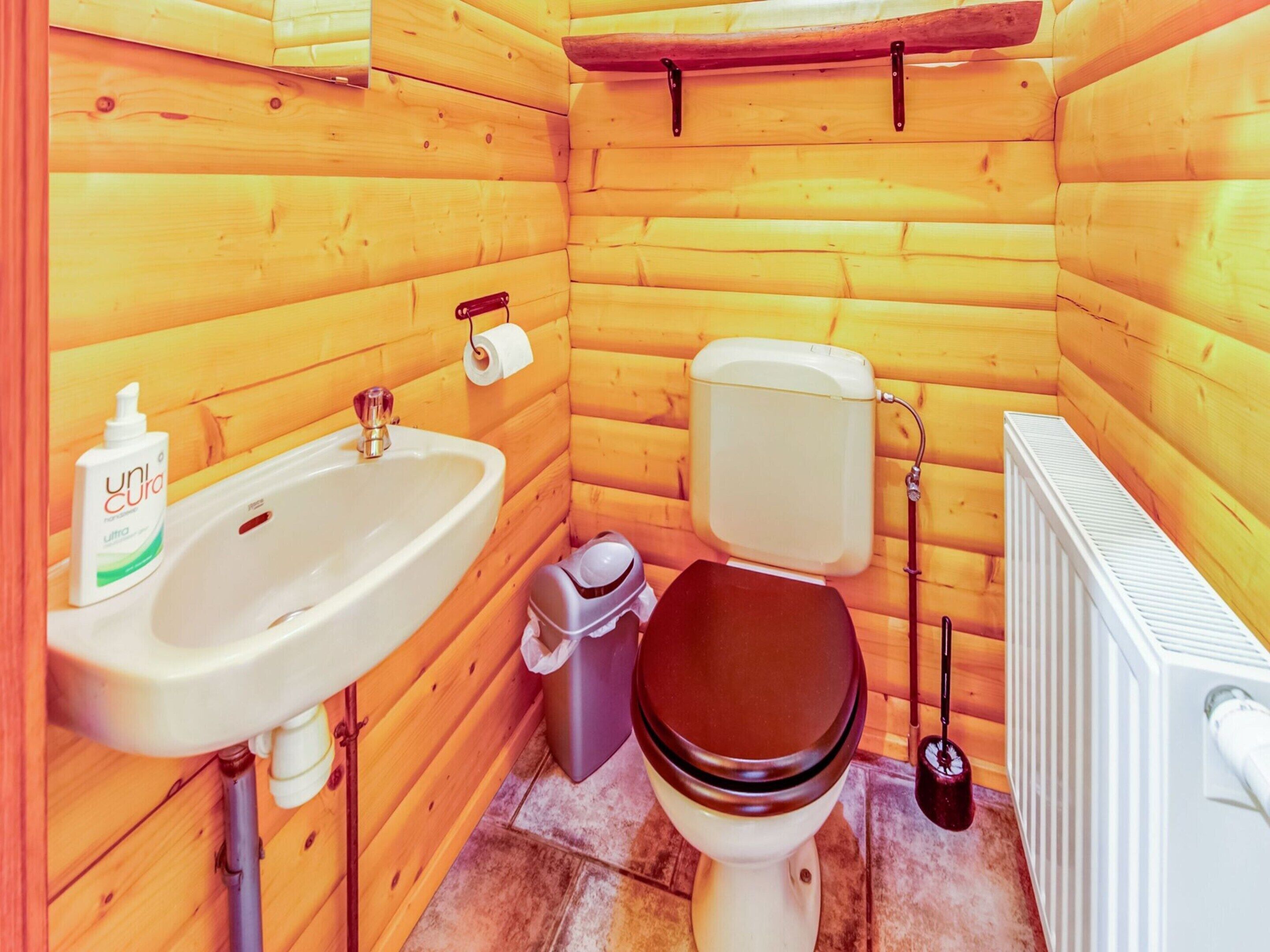 Ein kleines Badezimmer aus Holz mit Waschbecken, Toilette und Heizkörper.