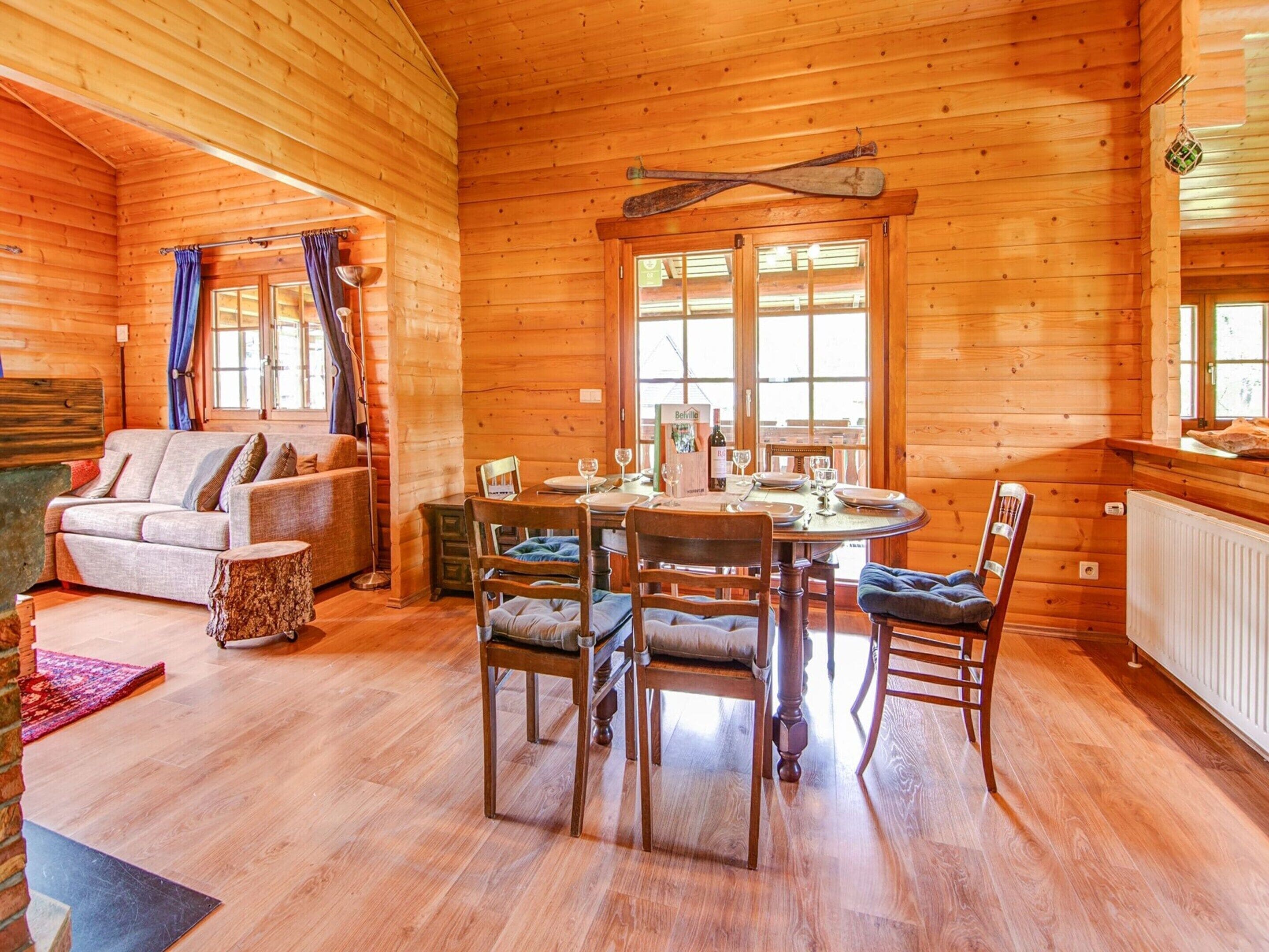 A wooden cabin interior with a dining area, a sofa, and a fireplace.