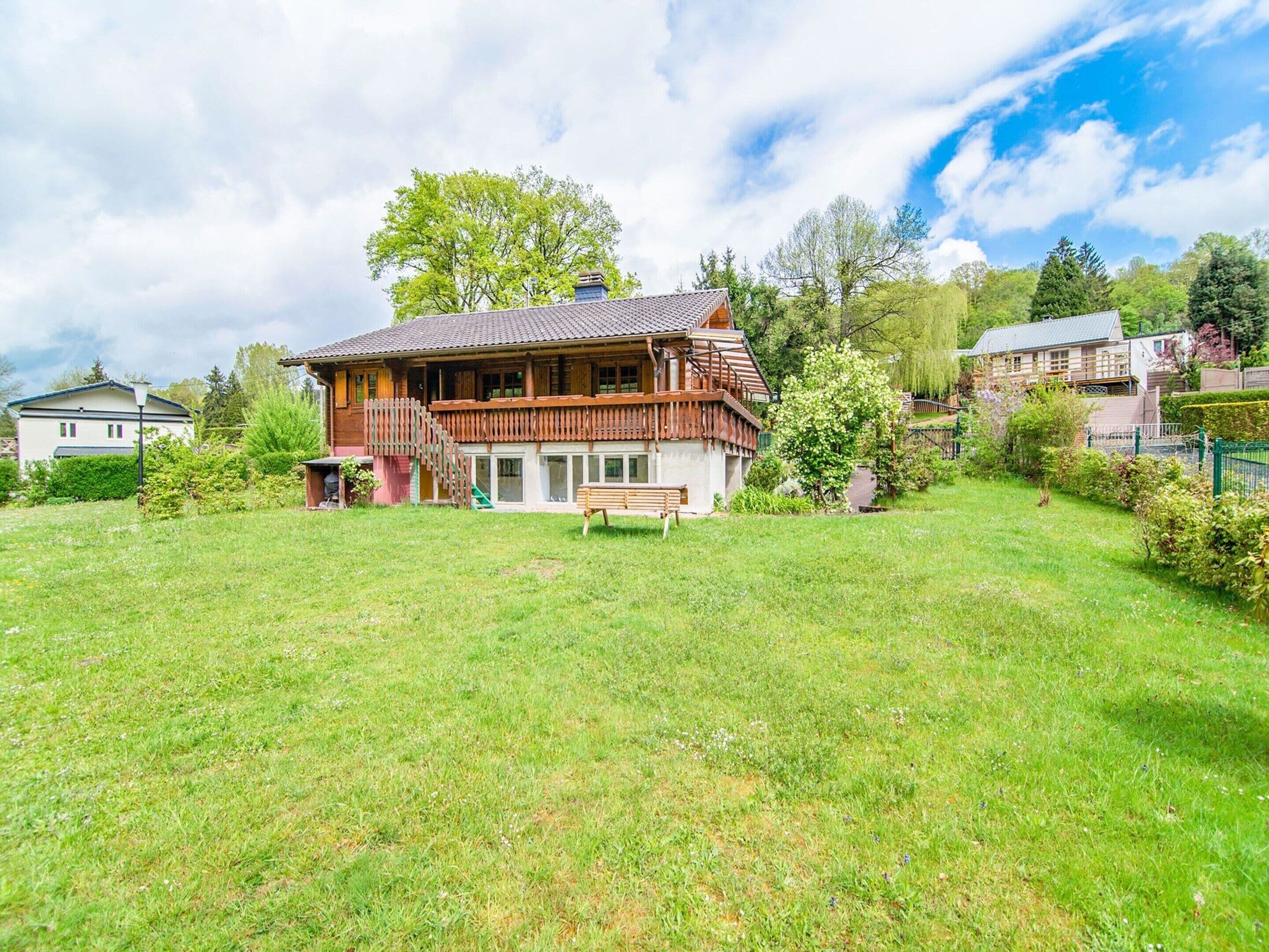 A large wooden house with a balcony, surrounded by a grassy yard and trees.