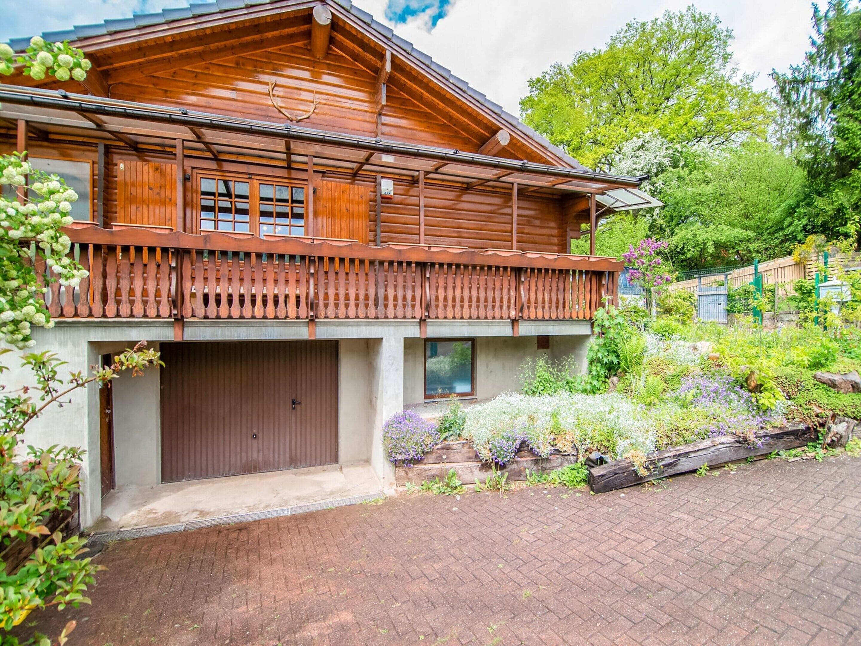 A wooden cabin with a balcony, a garage, and a garden.