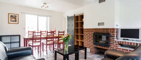 A living room with a fireplace, leather sofas, a dining area with wooden chairs, and a TV mounted on the wall.
