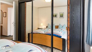 A bedroom with a large sliding door, a bed with patterned bedding, and a bedside table with a lamp. - Cozy Apartment in Wismar near Baltic Sea (Wismar)