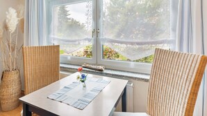 A room with a large window, wicker chairs, a table with a placemat, and a vase with flowers. - Cozy Apartment in Wismar near Baltic Sea (Wismar)
