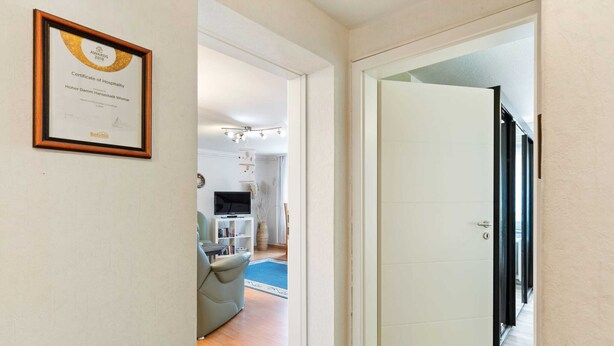 A hallway leading to a living area with a framed certificate on the wall, a sofa, and a TV. - Cozy Apartment in Wismar near Baltic Sea (Wismar)