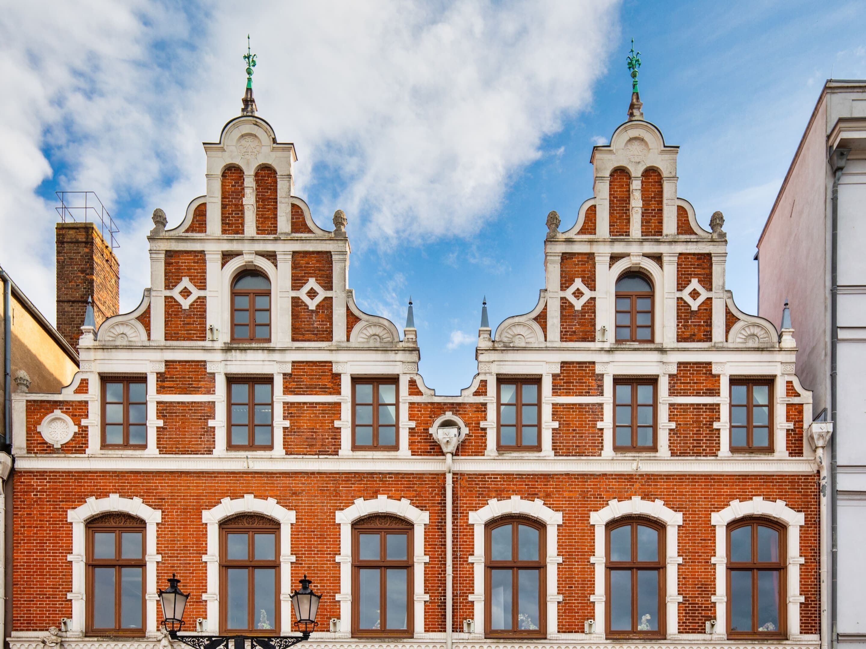 Ein historisches Gebäude mit einer symmetrischen Fassade, das gewölbte Fenster und schmuckes Backsteinmauerwerk aufweist.