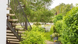 A garden patio area with a stone staircase leading to a white door, surrounded by lush greenery and a small table with chairs. - Cozy Apartment in Wismar near Baltic Sea (Wismar)