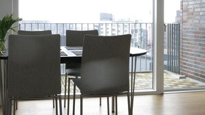 A dining area with a table and chairs, a potted plant, and a view of a cityscape through large windows. - Penthouse in Sydhavn 1135-1 (Copenhagen)
