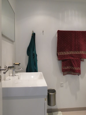 A bathroom with a white sink, a mirror, a towel rack with a teal robe, and a red patterned towel. - Penthouse in Sydhavn 1135-1 (Copenhagen)