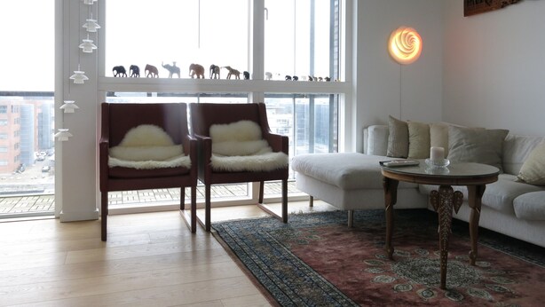 A modern living room with a large window, two armchairs, a sofa, a patterned rug, and a decorative wall piece. - Penthouse in Sydhavn 1135-1 (Copenhagen)
