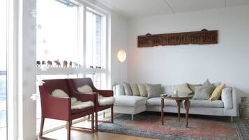 Una sala de estar con un sofá blanco, un sillón rojo, una mesa de centro de madera y una alfombra estampada.