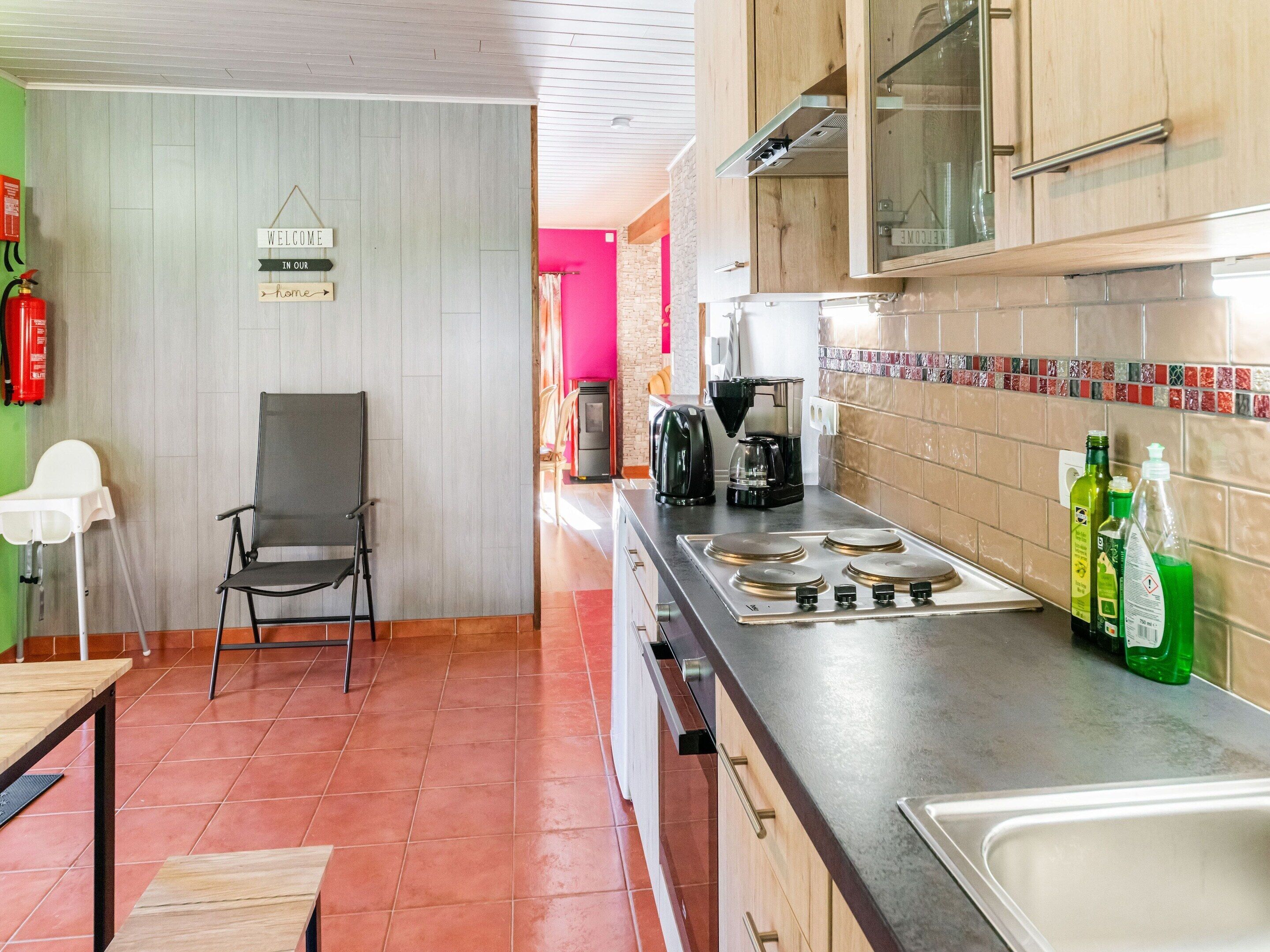 Una cocina con estufa, cafetera y una silla.