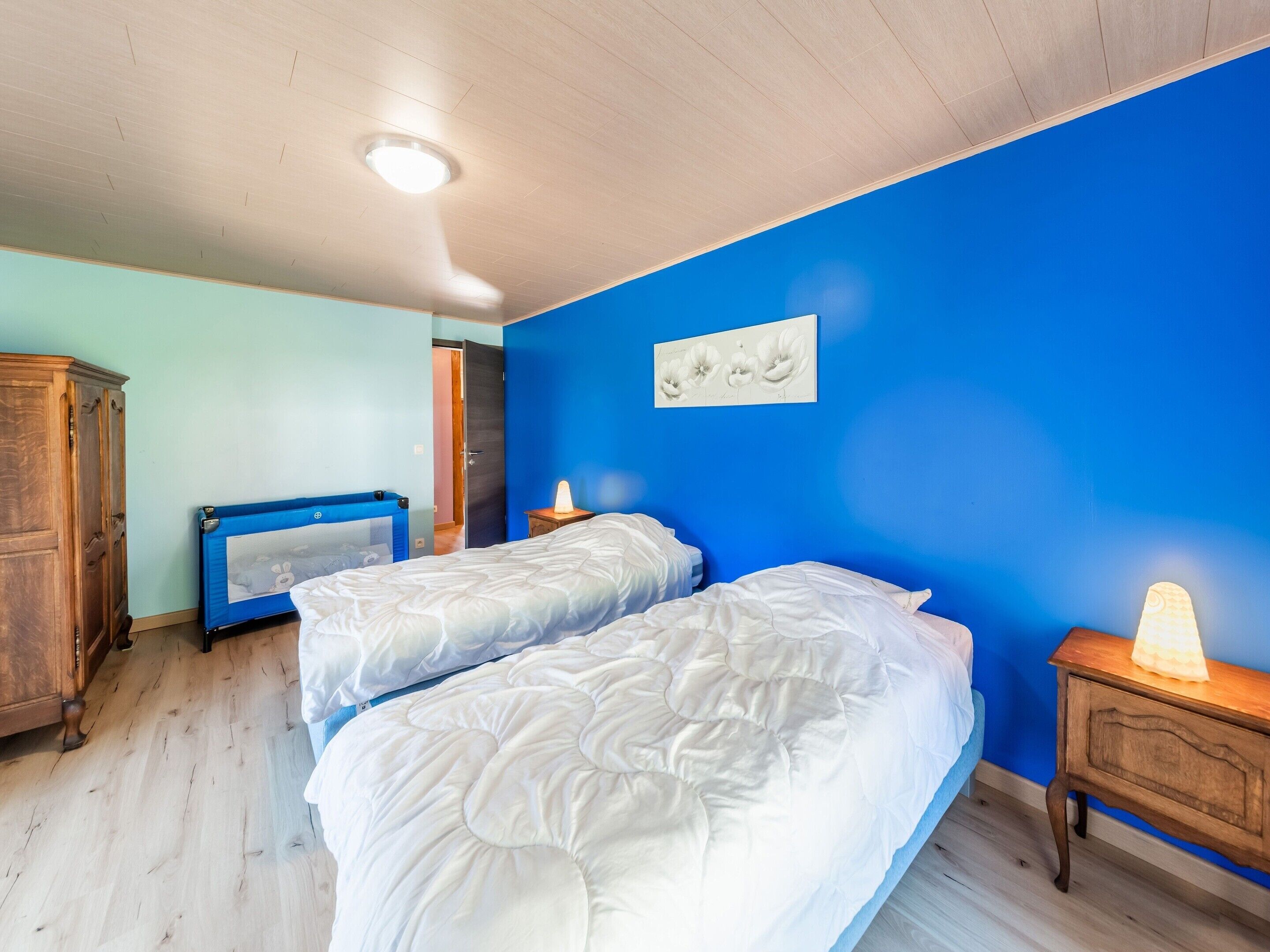 Ein Schlafzimmer mit zwei Betten, einem Holzschrank, einer blauen Wand und einer Deckenleuchte.