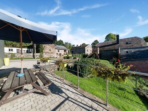 A courtyard with a picnic table, a covered area, stone buildings, and a fenced garden. - Holiday Home in Houffaliz With Garden (Houffalize)
