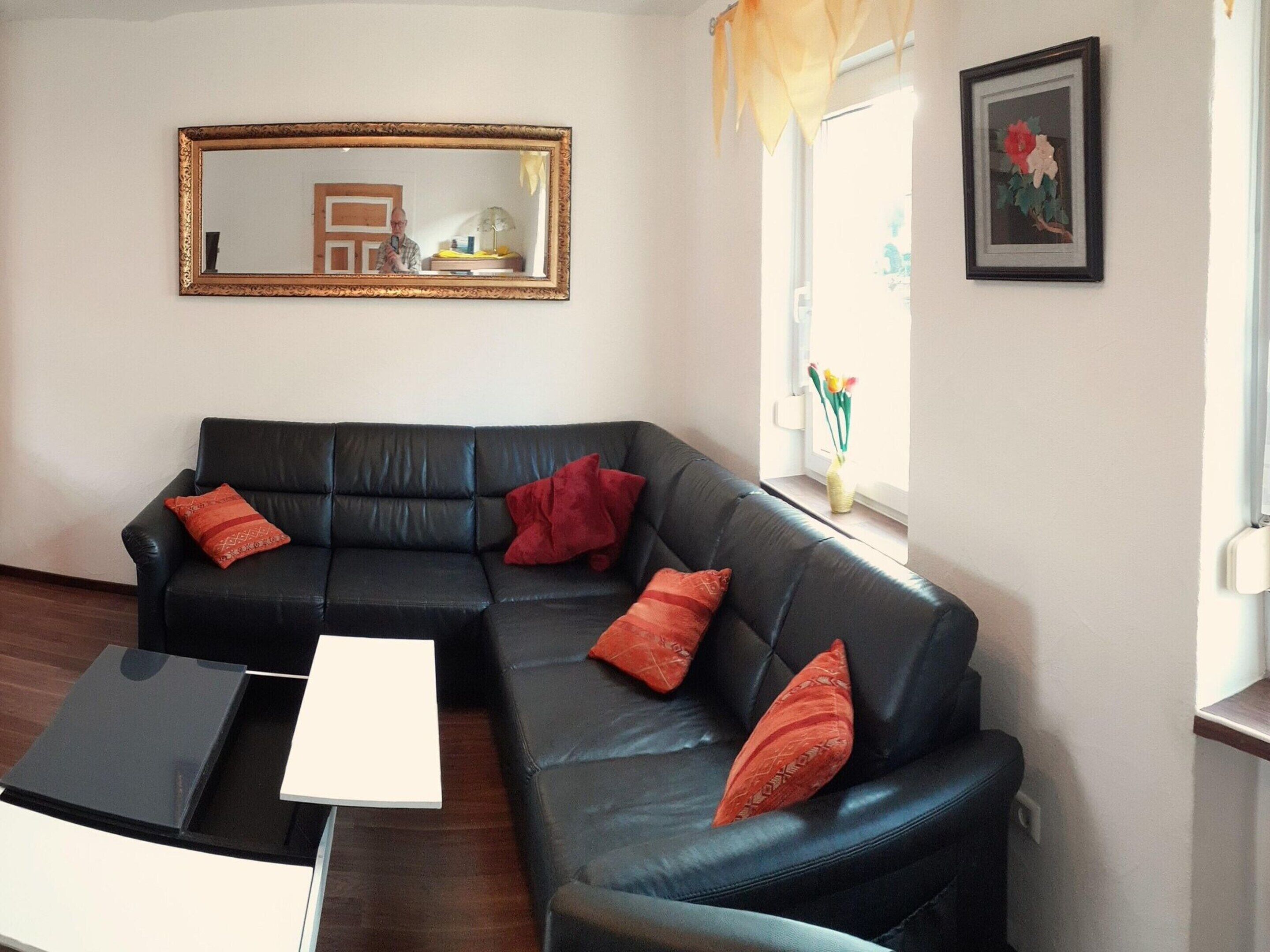 A living room with a black leather sofa, a white side table, and a framed mirror on the wall.