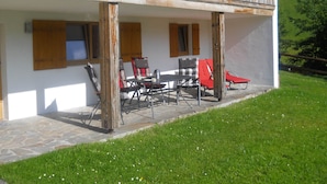 A wooden balcony with outdoor seating, a stone-paved area, and a grassy lawn. - Cozy Chalet in Niederndorf bei Kufstein near Ski Area (Niederndorferberg)