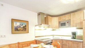 A small kitchen with wooden cabinets, a microwave, and a coffee maker. There is a dining table with plates and cups. - Cozy Chalet in Niederndorf bei Kufstein near Ski Area (Niederndorferberg)
