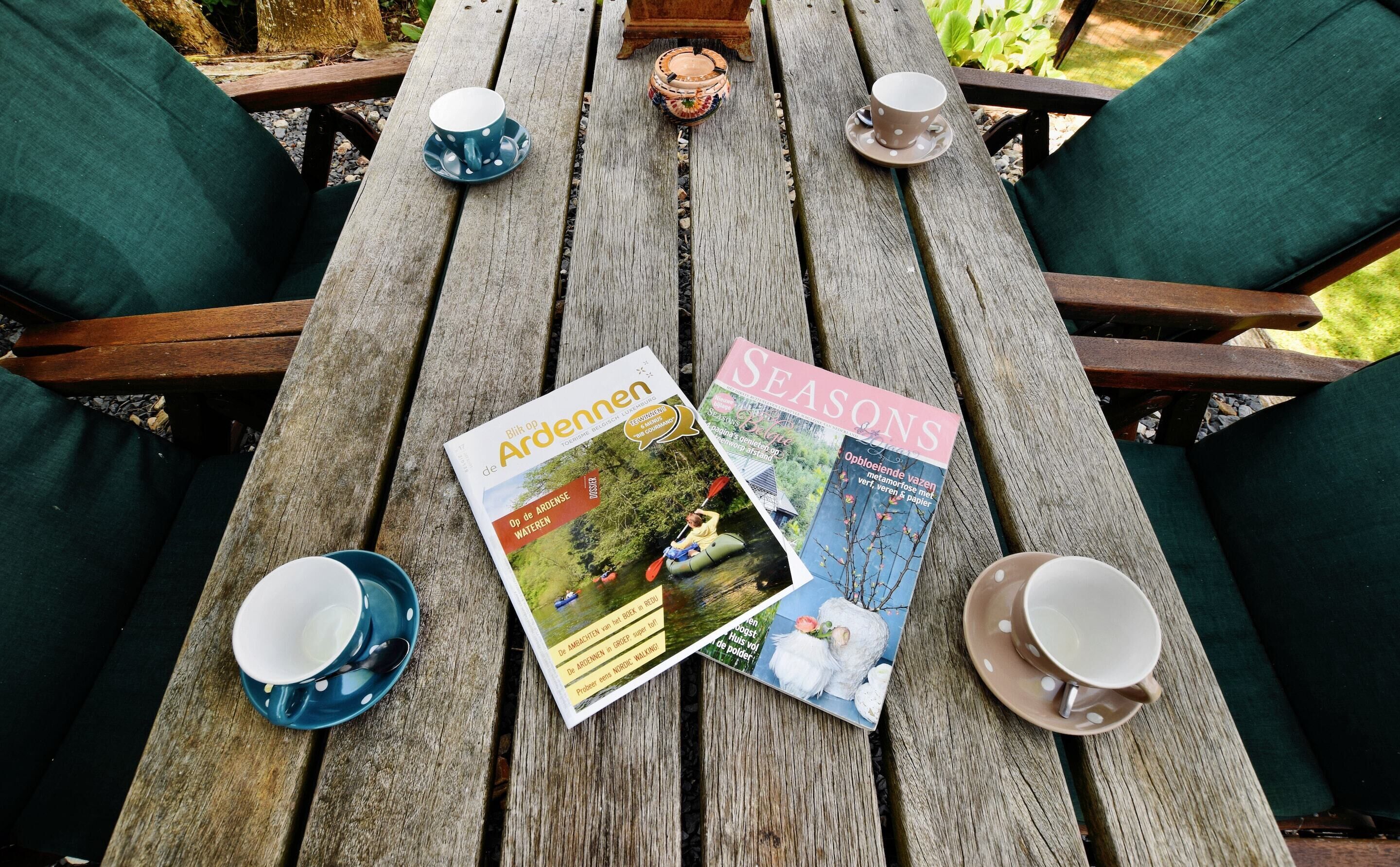 A wooden table with magazines, cups, and saucers.