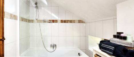 A bathroom with a glass-enclosed shower, a white bathtub, and a shelf with towels and toiletries.