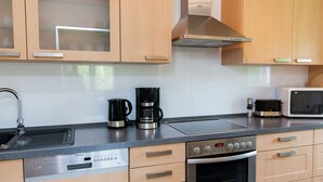 Une cuisine moderne dotée de meubles en bois, d’une hotte en acier inoxydable, d’un lave-vaisselle encastré, d’un four à micro-ondes et d’une machine à café.