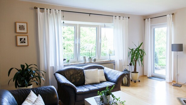 Un salon moderne avec un canapé en cuir, une table basse en bois et une grande fenêtre agrémentée de rideaux.