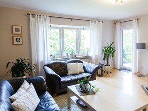 A modern living room with a leather sofa, a wooden coffee table, and a large window with curtains. - Cozy Apartment in Niederehe Eifel near Forest (Üxheim)