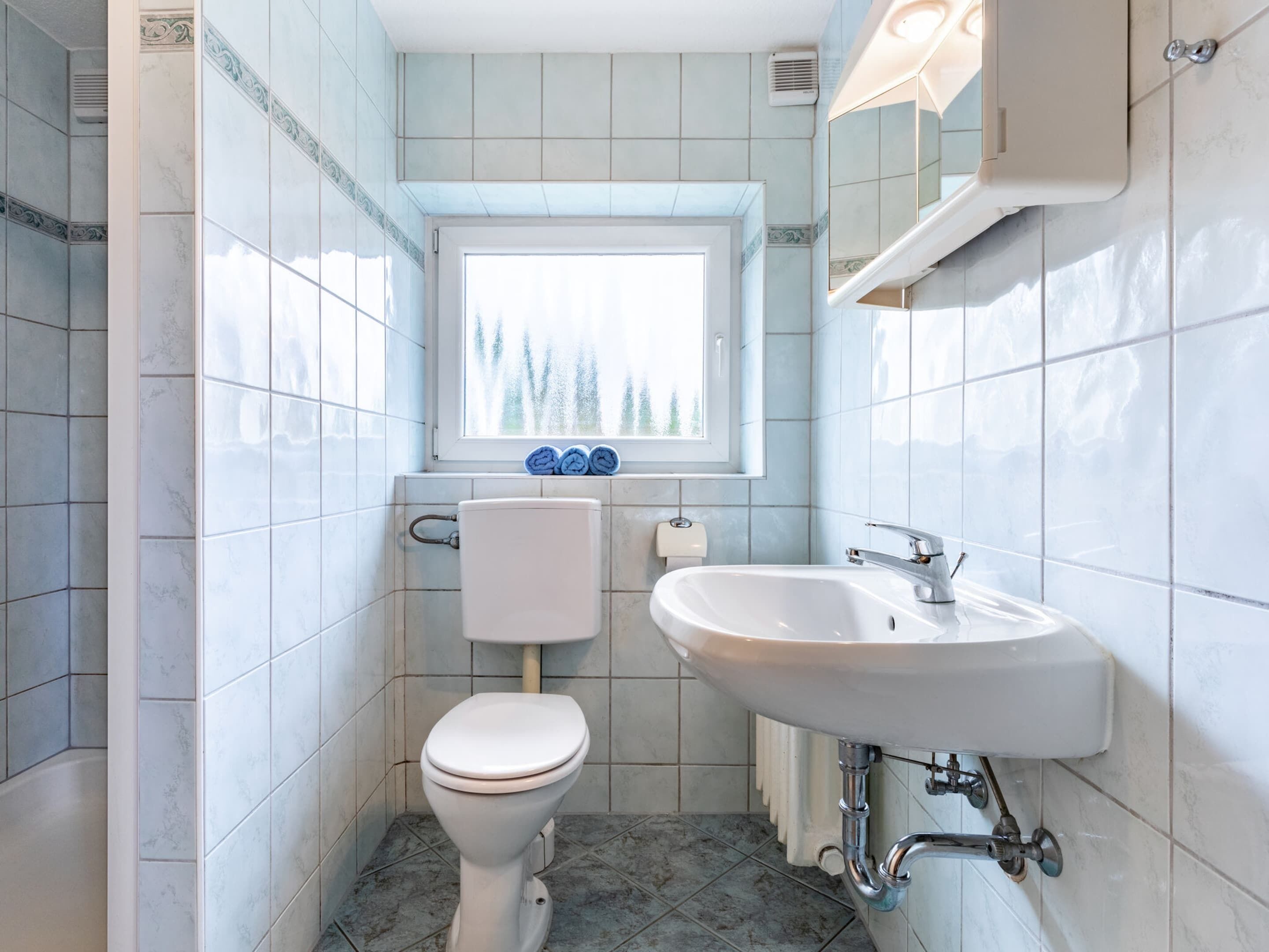 A bathroom with a toilet, sink, and window.