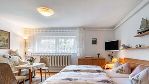 A hotel room with a bed, a desk, a chair, a radiator, a TV, and a window with curtains.