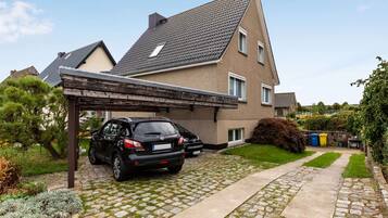 Ein Wohnhaus mit befestigter Auffahrt, überdachtem Carport und einem Garten mit Sträuchern und Rasen.