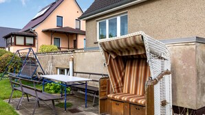 A patio with a swing set, a table, and a wicker bench with a striped cushion.