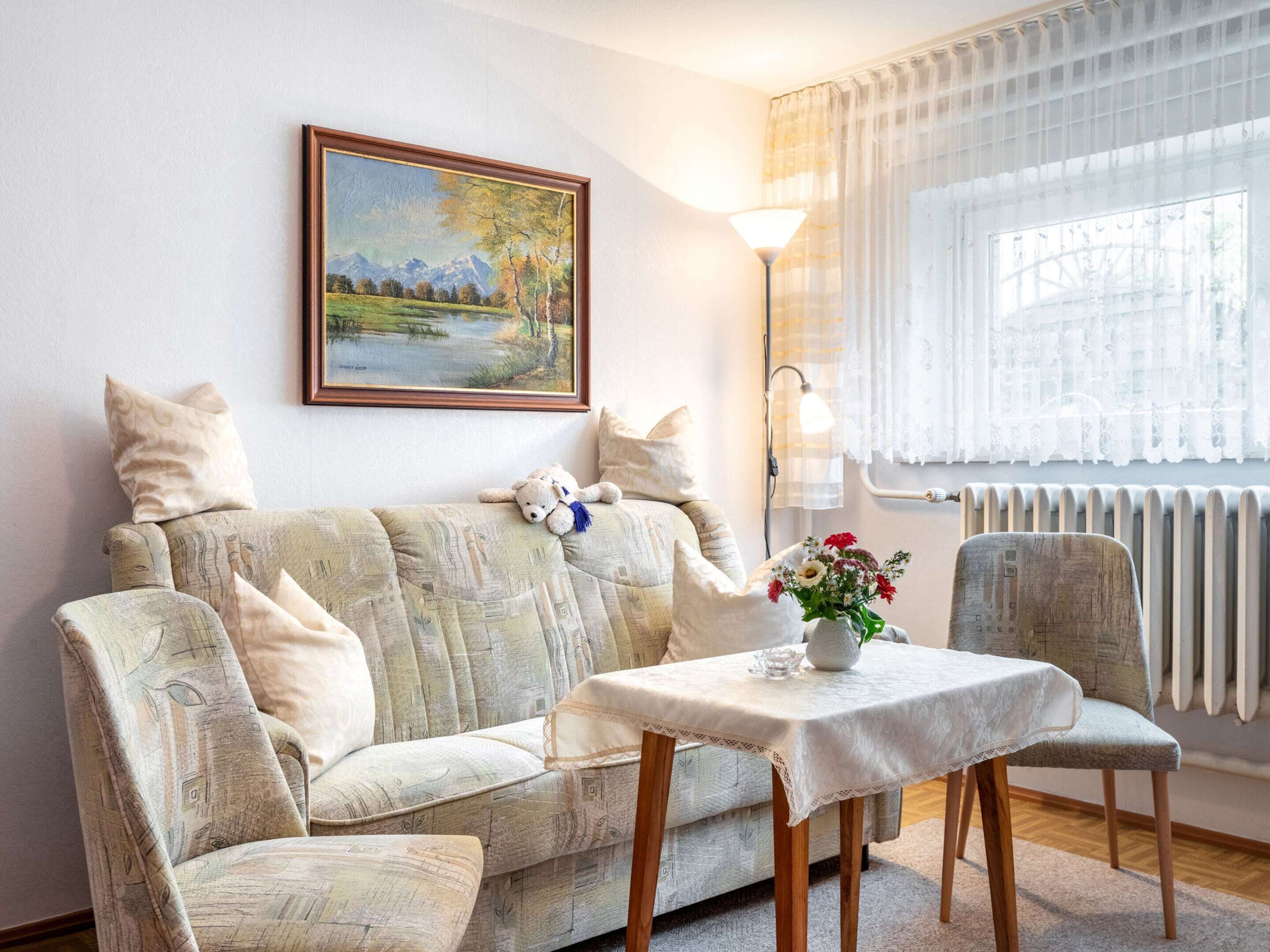 Un salon chaleureux avec un canapé, une petite table sur laquelle est posé un vase de fleurs, une lampe et un tableau accroché au mur.